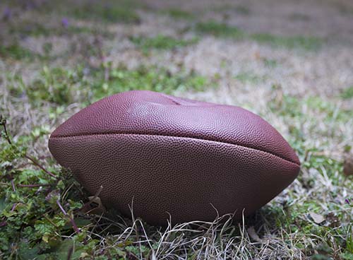 a flat football laying on a wilted field