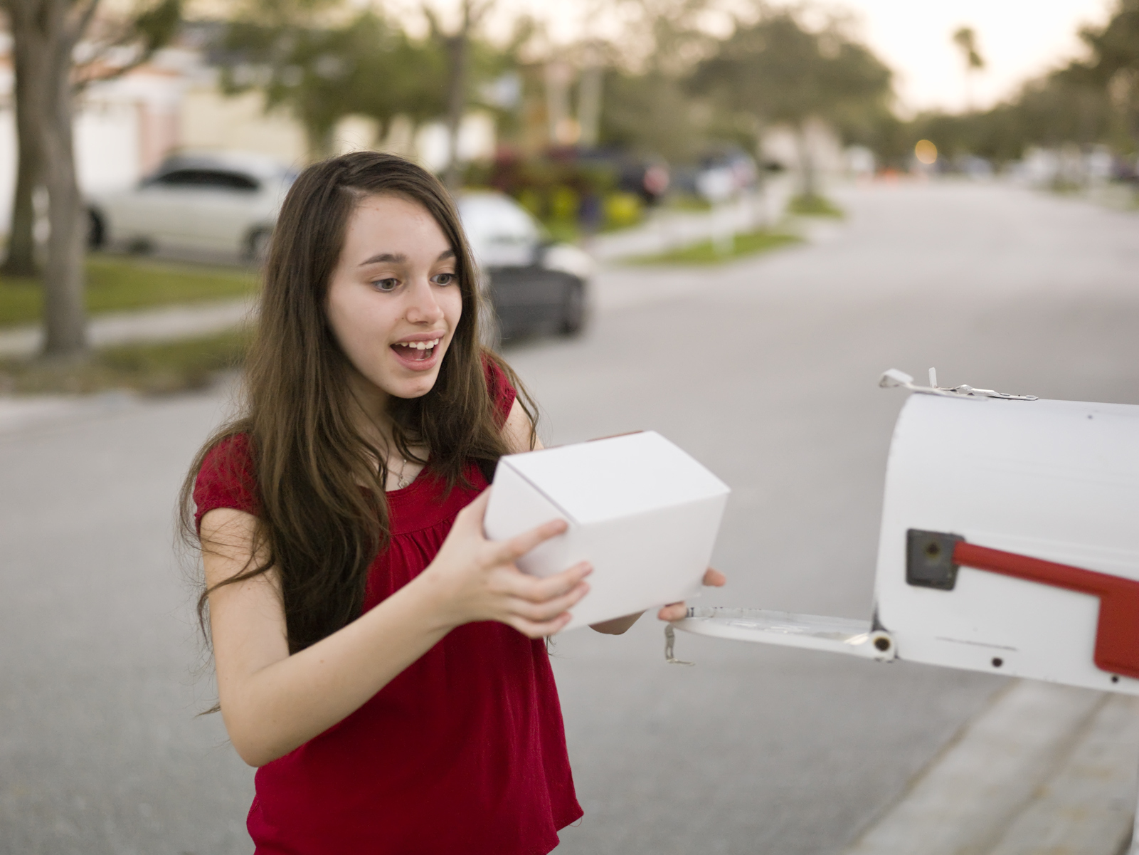 a young girl takes a package out of a mailbox with an expression of excitement
