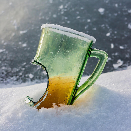 A broken and melted pint glass sits partially buried in a snowdrift