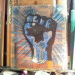 a painting of a blue solidarity fist hangs in a cluttered art studio