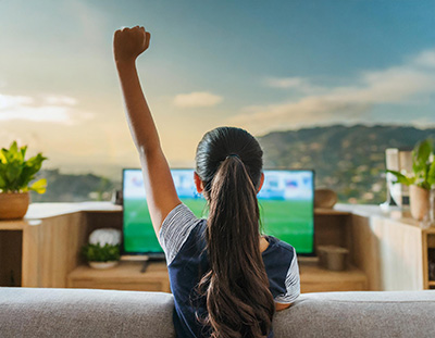 a teenage girl on a couch watching a sports event holds up her fist in triumph