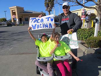 two kids hold up a protest sign reading "toca tu vocina"