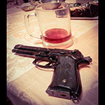 a black handgun rests on a wood table in front of a mostly-drunk stein of beer. 