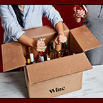 two white women in sweaters unload a box labeled "winc" that is full of wine.