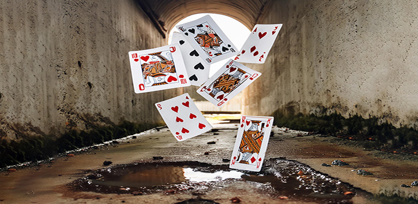 In a dirty, wet concrete tunnel, a handful of playing cards are flying through the air.