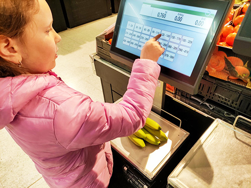 A young girl weighs bananas on an electronic scale in a supermarket.